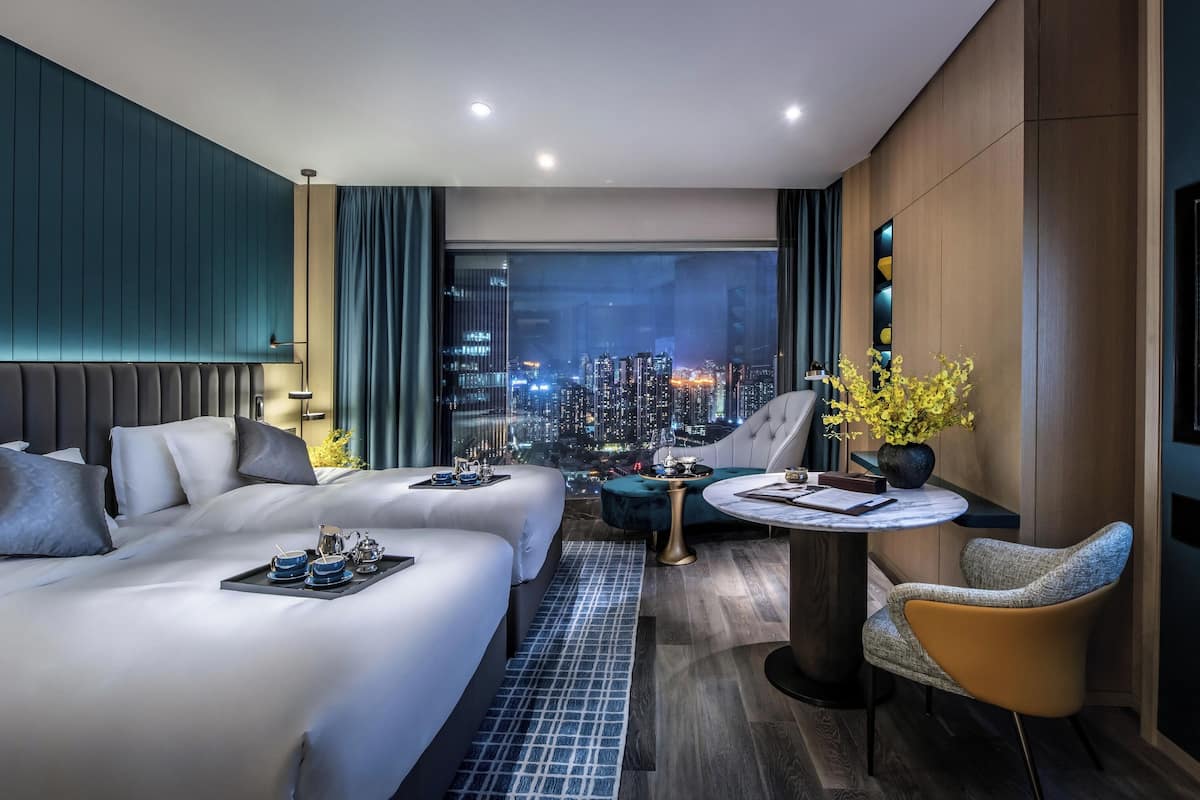 Una habitación de hotel moderna con vista a la ciudad, un sofá cama, una mesa de comedor y una pantalla de televisión.
