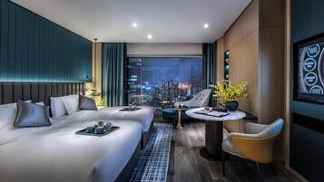 A modern hotel room with a city view, a sofa bed, a dining table, and a TV screen.