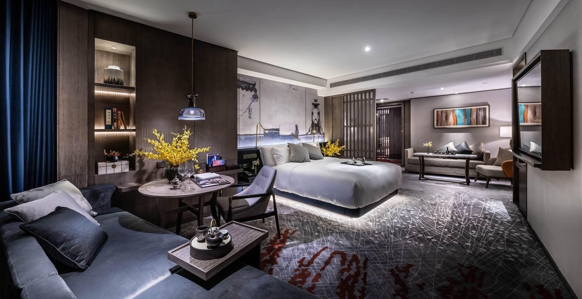 A modern hotel room with a large bed, a sofa, a desk, and a dining area.