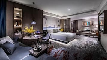 A modern hotel room with a large bed, a sofa, a desk, and a dining area.