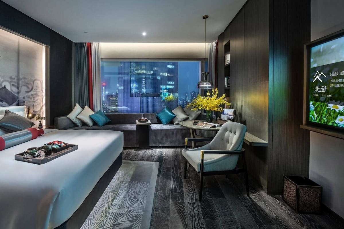 Una habitación de hotel moderna con una cama grande, un sofá, un escritorio y vistas a la ciudad de noche.