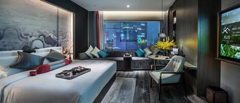 A modern hotel room with a large bed, a sofa, a desk, and a view of the city at night.