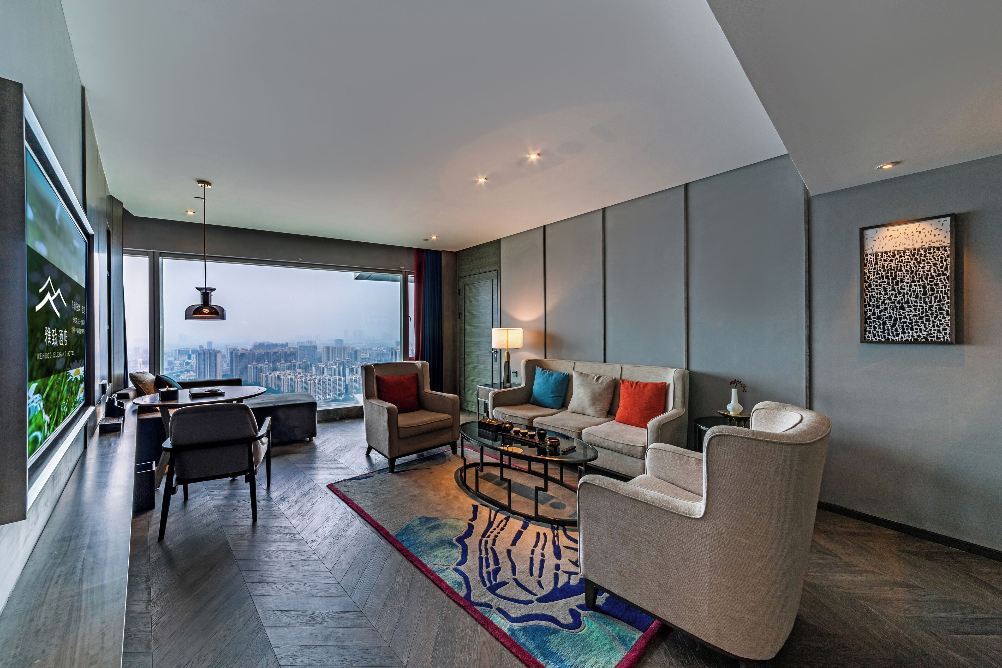 A modern living room with a sofa, armchairs, a coffee table, and a view of the city through large windows.
