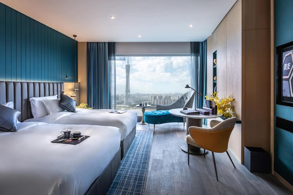 Una habitación de hotel moderna con dos camas, una zona de estar y un ventanal con vistas a la ciudad.