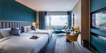 Una habitación de hotel moderna con dos camas, una zona de estar y un ventanal con vistas a la ciudad.