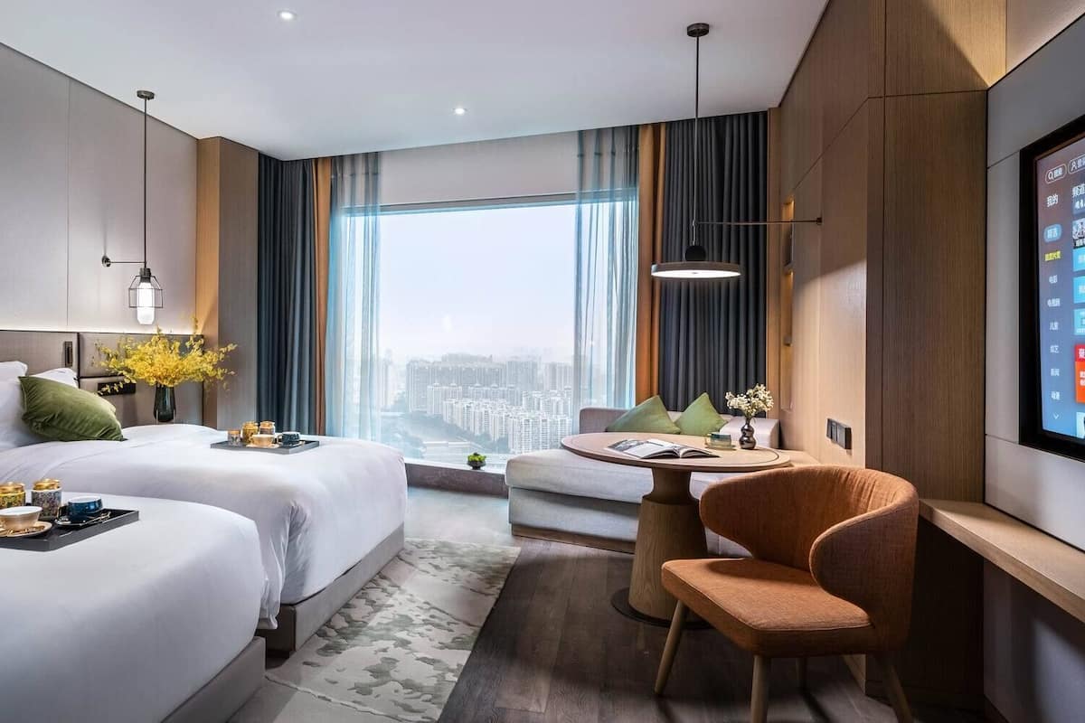 Una habitación de hotel moderna con dos camas, una mesa de comedor, una silla y un televisor.