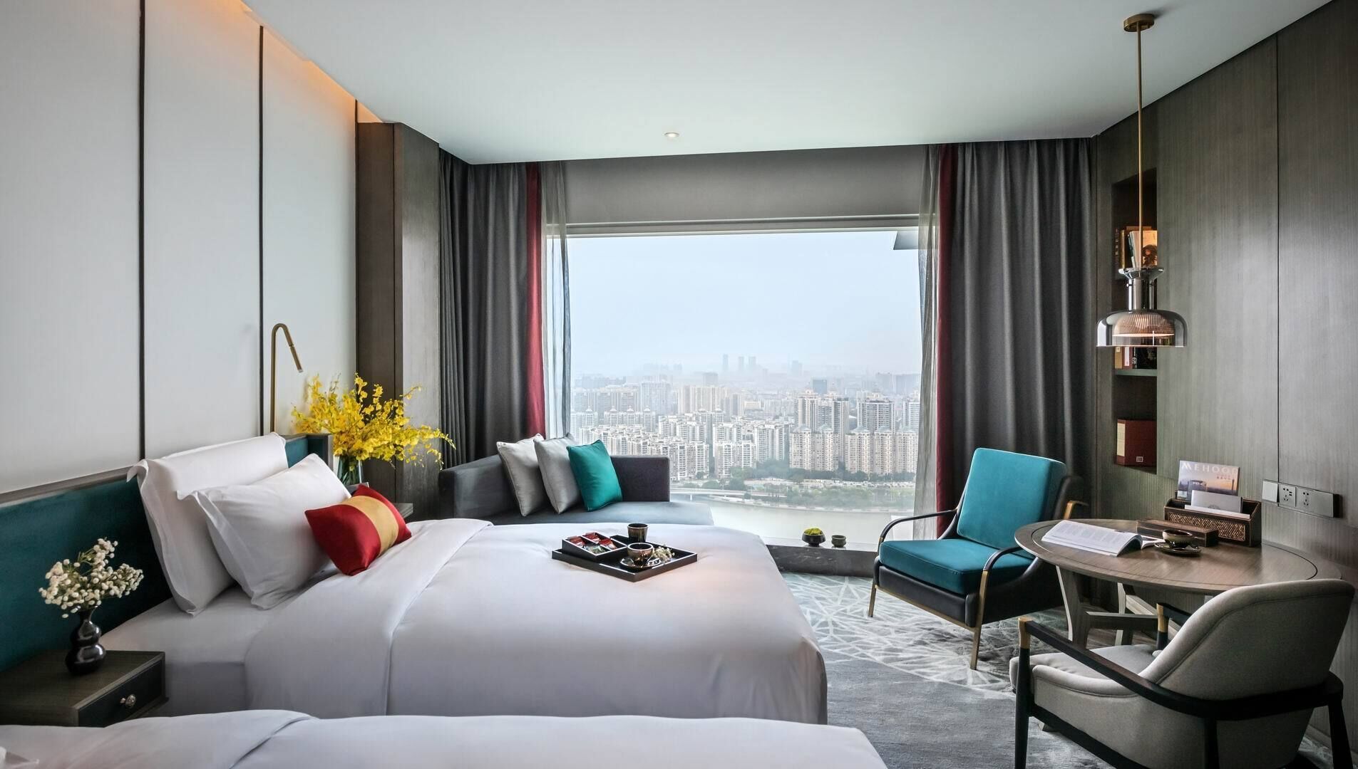 A modern hotel room with a large bed, a desk, and a view of a cityscape.