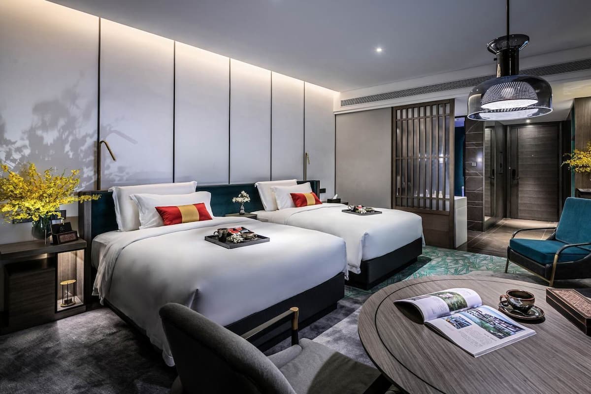 Una habitación de hotel moderna con dos camas, una zona de estar con una mesa y un televisor.