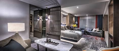 A modern hotel room with a sofa, a dining table, a bed, and a seating area.