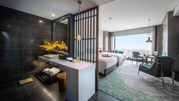 A modern hotel room with a large bed, a sitting area with a desk, a bathroom with a vanity and a large mirror, and a city view.