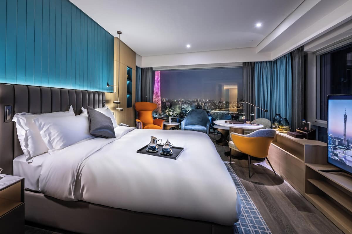 Una habitación de hotel moderna con una cama grande, un escritorio y vista a la ciudad de noche.