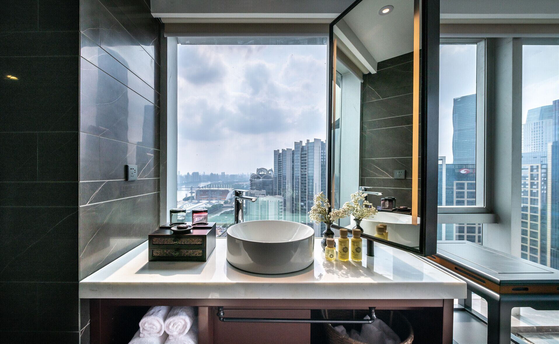 A modern bathroom with a large window, a round sink, and a mirror.