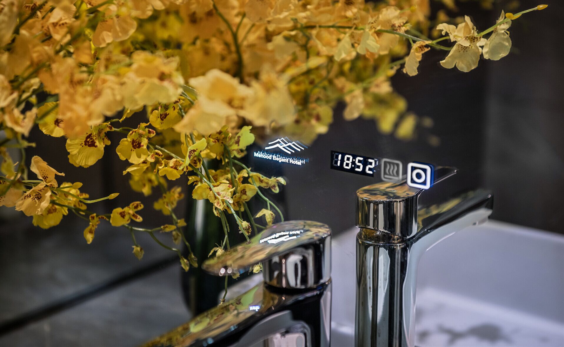 A bathroom with a modern faucet and a digital clock displaying 18:52.