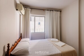 Une chambre à coucher avec un lit, des rideaux, une fenêtre et un appareil de climatisation.