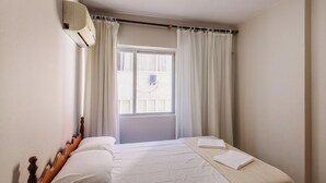 Une chambre à coucher avec un lit, des rideaux, une fenêtre et un appareil de climatisation.