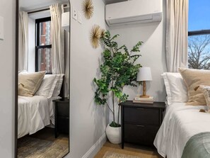 A bedroom with a bed, bedside tables, a potted plant, a lamp, and a mirror.