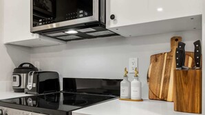 Una cuina moderna amb fogó, microones, torradora i taula de tall de fusta.