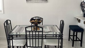 A dining area with a glass table, black chairs, a decorative bowl centerpiece, and a wall-mounted air conditioner. - Brand new 2-bedroom cottage, Harts Exuma across the street from the beach (Exuma)