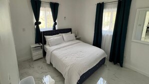 A bedroom with a bed, nightstands, a ceiling fan, and curtains. - Brand new 2-bedroom cottage, Harts Exuma across the street from the beach (Exuma)