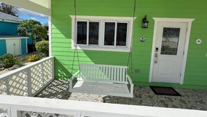 A porch with a white swing, a white door with a glass panel, and a small window above the door. - Brand new 2-bedroom cottage, Harts Exuma across the street from the beach (Exuma)