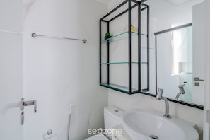 Un bagno moderno con un lavandino bianco, uno scaffale in vetro e uno specchio con cornice nera.