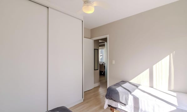 A bedroom with two beds, a ceiling fan, and a view of the hallway.