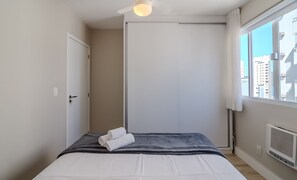 A bedroom with a bed, a door, a window with a view of buildings, and a ceiling fan.