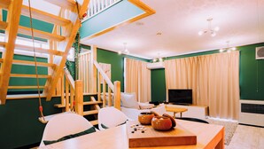 A cozy living room with a wooden staircase, a TV, and a dining area with a table set for two. - 3BD Yuzawa Onsen Lodge House A (Minamiuonuma)