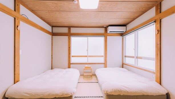 A small, minimalist room with two beds, a tatami mat floor, and a large window. - 3BD Yuzawa Onsen Lodge House A (Minamiuonuma)