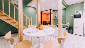 A dining area with a round table, chairs, and a fruit bowl. There is a staircase with wooden railings and a kitchen area with a microwave and toaster. - 3BD Yuzawa Onsen Lodge House A (Minamiuonuma)