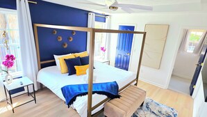 A bedroom with a four-poster bed, a bedside table, a bench, and a large window with curtains.