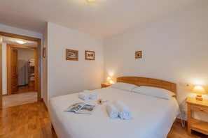 Quarto de hotel com uma cama grande, cabeceira de madeira, mesa de cabeceira com luminária e porta para um banheiro.