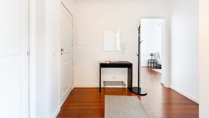 Un couloir avec une porte blanche, une console noire surmontée d’une petite étagère en fil métallique et un tapis gris.
