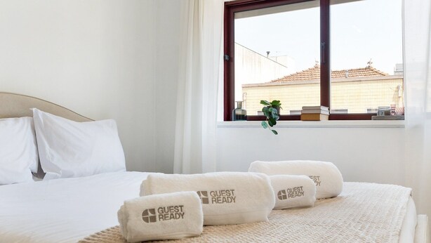 Une chambre d’hôtel avec un lit bien fait, du linge de lit blanc et une fenêtre donnant sur des immeubles.