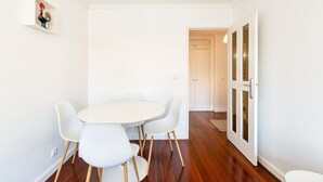Un espace repas avec une table ronde et quatre chaises blanches, un plancher en bois et des murs blancs.