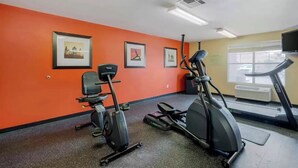A gym with orange walls, exercise equipment, and framed pictures. - Fully Furnished Hotel Suites in Las Vegas with Fitness Room and Outdoor Pool (Las Vegas)