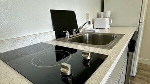 A modern kitchen with a black induction cooktop, stainless steel sink, and a white coffee maker. - Fully Furnished Hotel Suites in Las Vegas with Fitness Room and Outdoor Pool (Las Vegas)