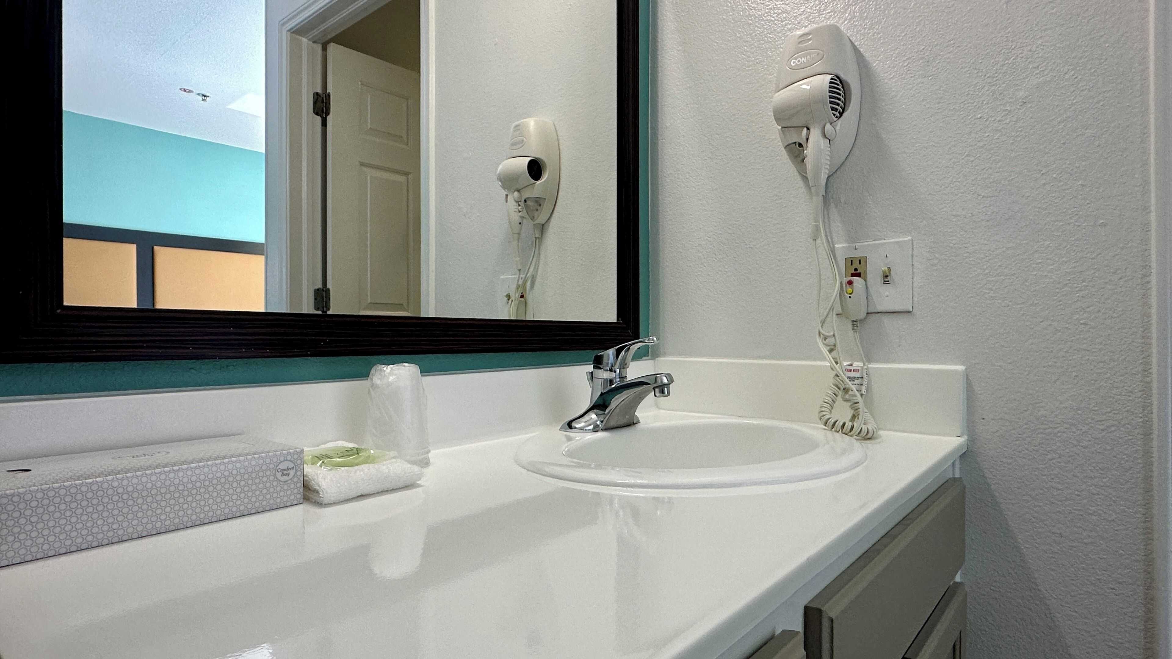 A bathroom with a white sink, a mirror, a hair dryer mounted on the wall, and a towel dispenser.