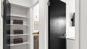 Un baño moderno con una puerta negra, paredes blancas y un estante empotrado con toallas dobladas.