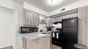 Una cocina moderna con una isla central, refrigerador negro y muebles de madera.
