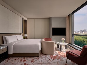 A modern hotel room with a large bed, a seating area with a chair and a small table, a TV mounted on the wall, and a view of a cityscape through large windows. - Intercontinental Changchun High Tech Zone (Changchun)