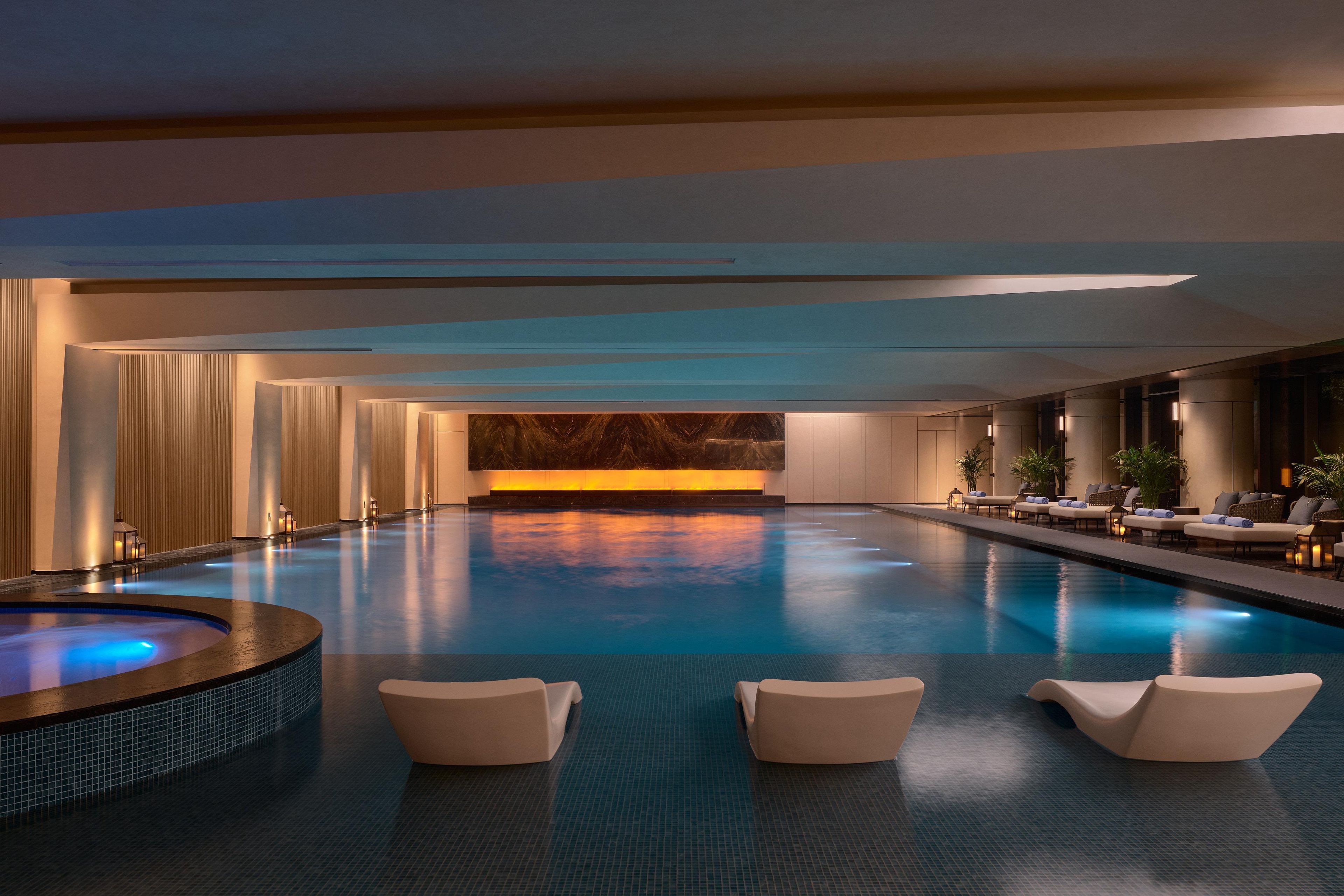 Une piscine intérieure spacieuse, dotée d’un jacuzzi, de chaises longues et d’un mur en marbre en arrière-plan.