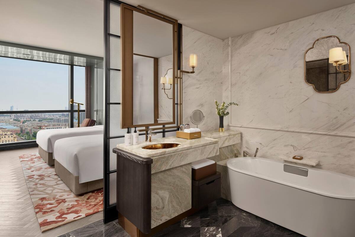 Een moderne hotelbadkamer met een grote spiegel, een badkuip en een wastafel met een marmeren aanrecht.