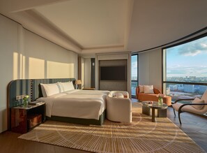 Una moderna camera d'albergo con un letto grande, due comodini, un’area salotto con divano e poltrone, un piccolo tavolino da caffè e un’ampia finestra con vista sulla città.