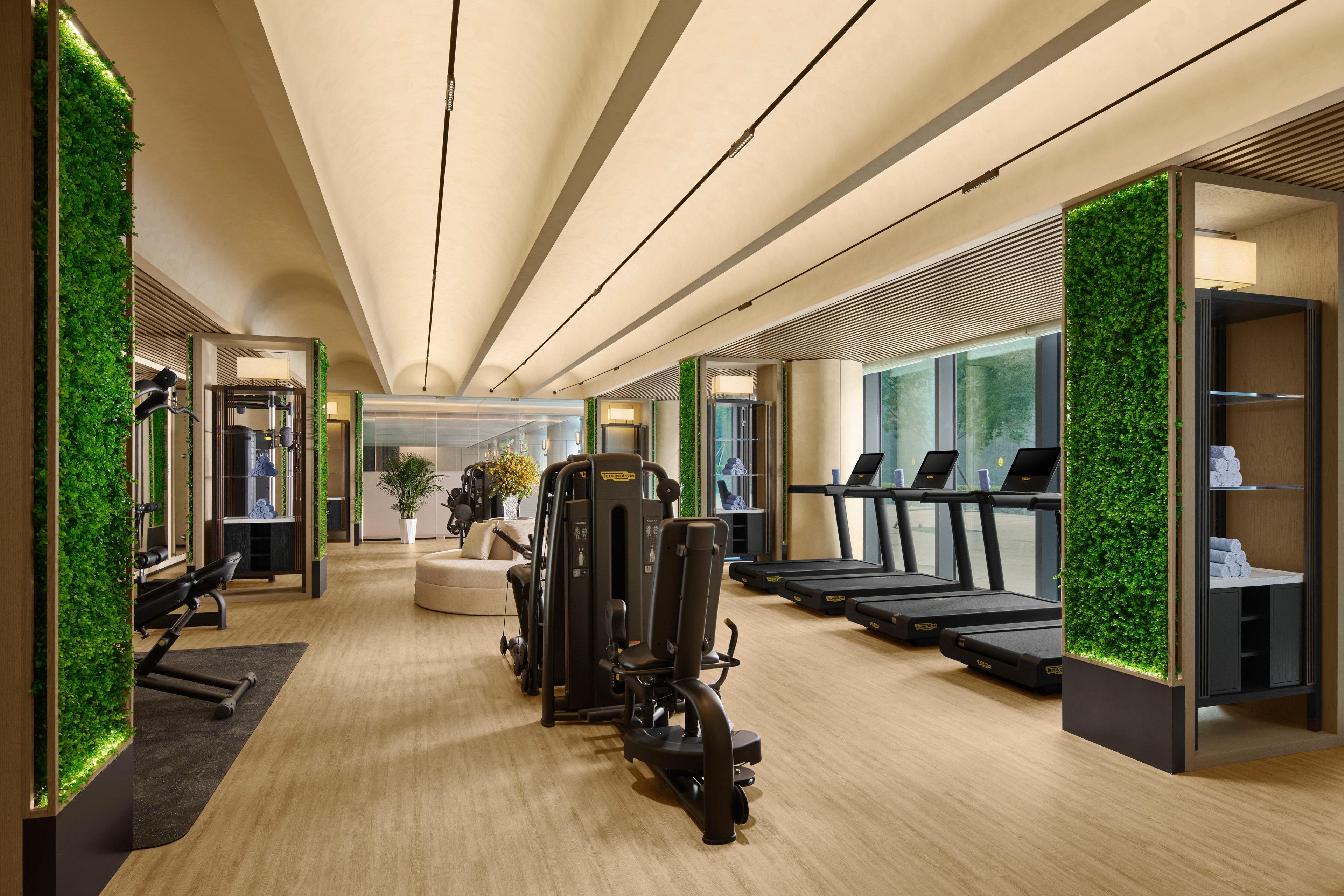 A modern gym with treadmills, weight machines, and a wall of green foliage.