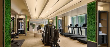 Un gimnasio moderno con cintas de correr, máquinas de pesas y una pared cubierta de follaje verde.