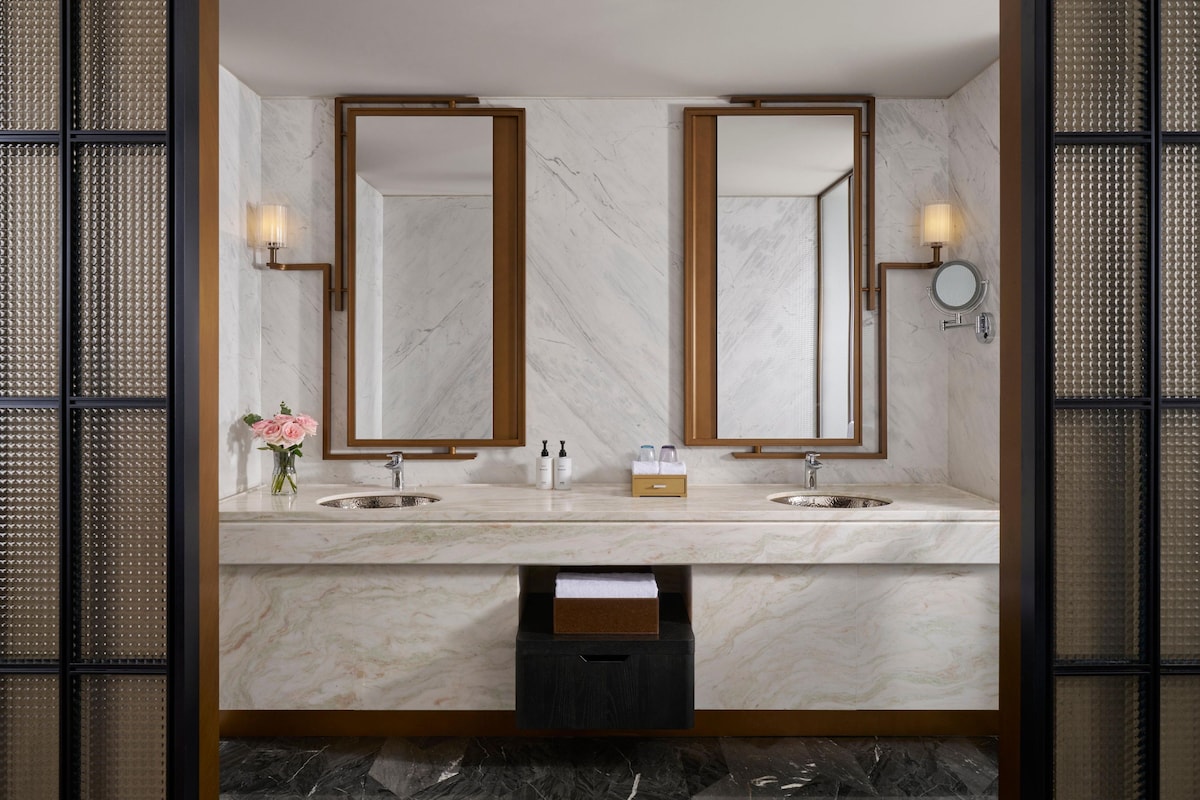 A bathroom with two sinks, large mirrors, and a small trash bin.