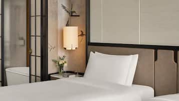 Quarto de hotel com cama, mesa de cabeceira com abajur, vaso com flores e um mural de aves na parede.