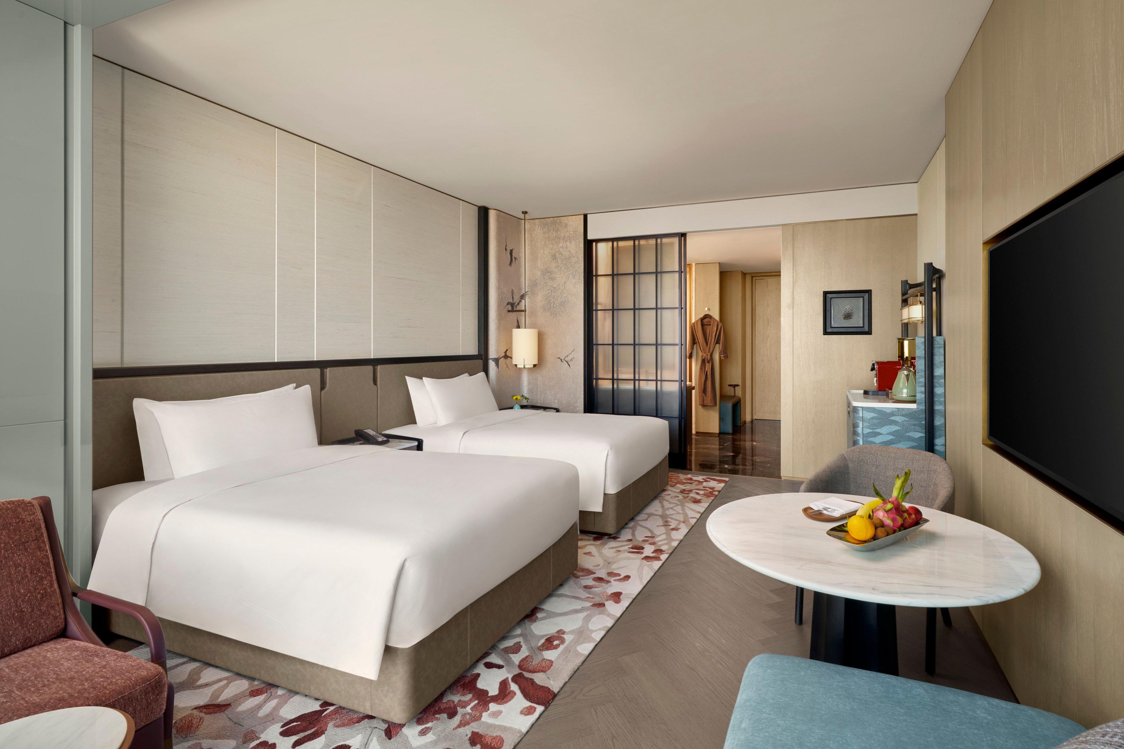 A hotel room with two beds, a seating area with a table, and a TV.