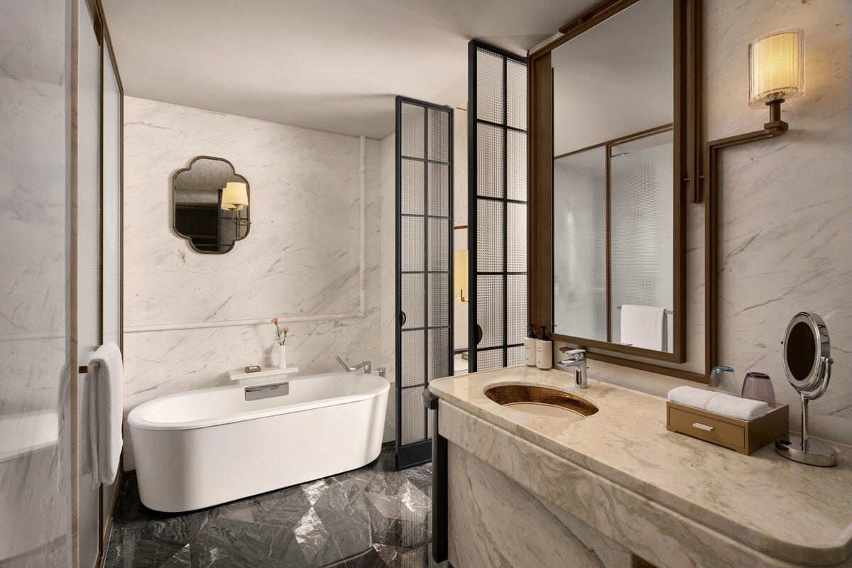 A modern bathroom with a freestanding bathtub, a large mirror, and a marble countertop.